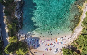 An aerial view of a beach with clear turquoise water, rocky shoreline, and a sandy area with beach umbrellas and people. - Sea Mare Stin Vista - swim up - B1 (Pula)