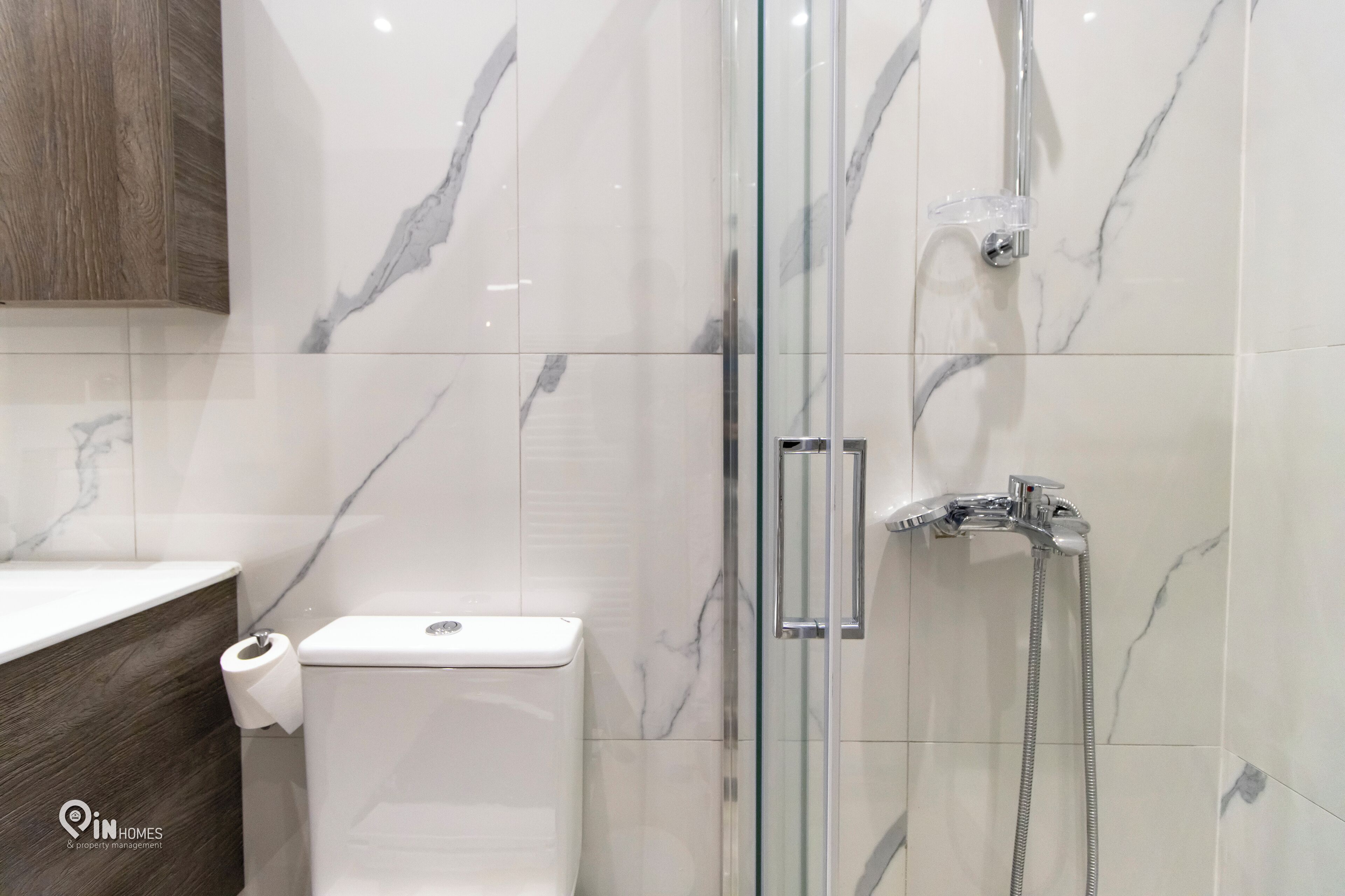 A bathroom with a glass-enclosed shower, a toilet, and a wooden vanity.