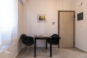 A small room with a dining table and two chairs, a framed picture on the wall, a door, and a thermostat. - Apollon - Premium Studio Near Metro Athens (Athina)