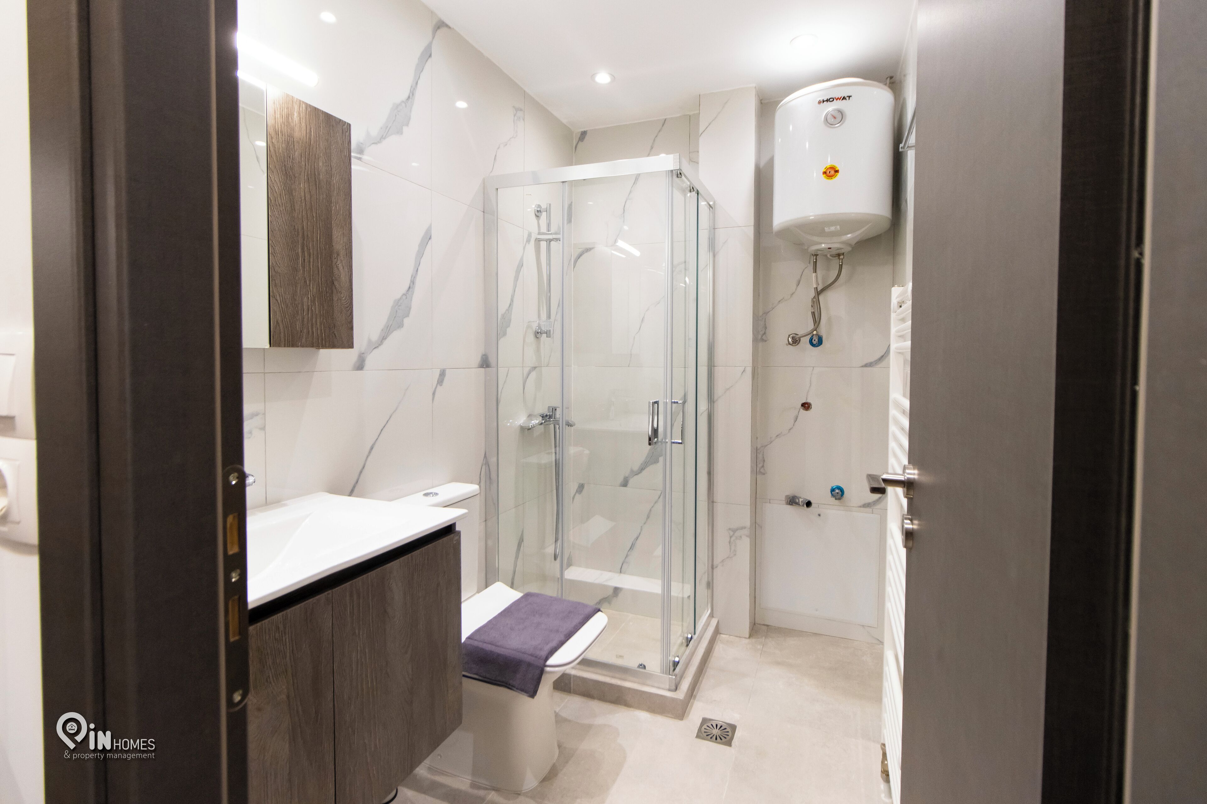 A modern bathroom with a glass-enclosed shower, a white sink, and a marble-tiled wall.