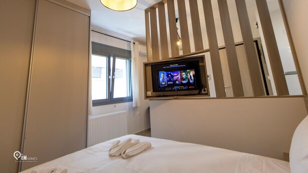 Una habitación de hotel con cama, televisor montado en la pared, ventana con cortinas e iluminación en el techo.