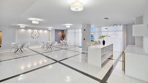 Een moderne hotellobby met een receptiebalie, een zithoek en grote ramen.