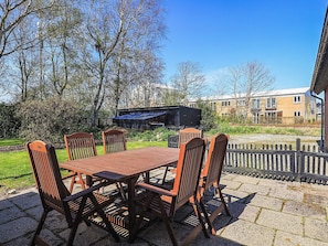 Een terras buiten met een houten tafel en stoelen, een barbecue en uitzicht op een woongebied met huizen en een spoorlijn.