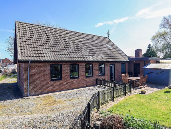 Een gebouw van baksteen met een pannendak, een grindpad en een omheind buitengebied.