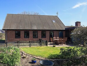 Een bakstenen huis met pannendak, een omheind erf en een tafel met stoelen buiten.