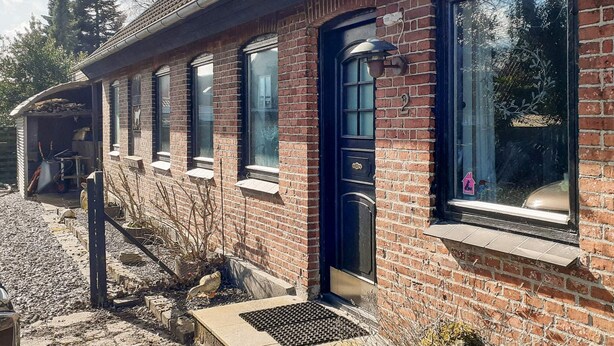 Un bâtiment en briques avec une porte noire, des fenêtres et un petit porche.