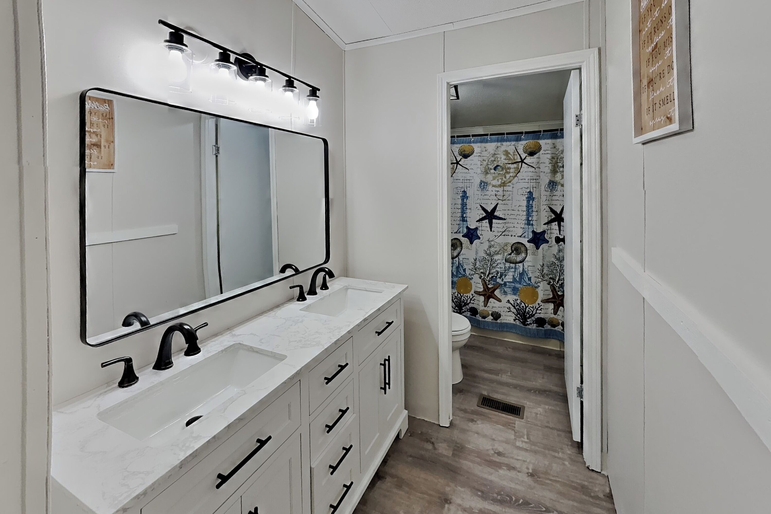 Een badkamer met een wit wastafelmeubel, twee wastafels, een grote spiegel en een douche met een blauw-wit betegeld ontwerp.