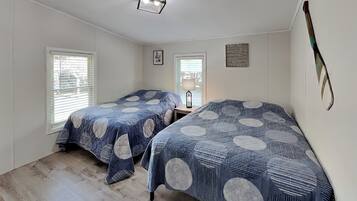 Een slaapkamer met twee bedden, houten vloeren en een plafondlamp.