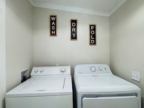 A laundry room with two white washing machines and three wooden signs labeled 'WASH,' 'DRY,' and 'FOLD' on the wall.