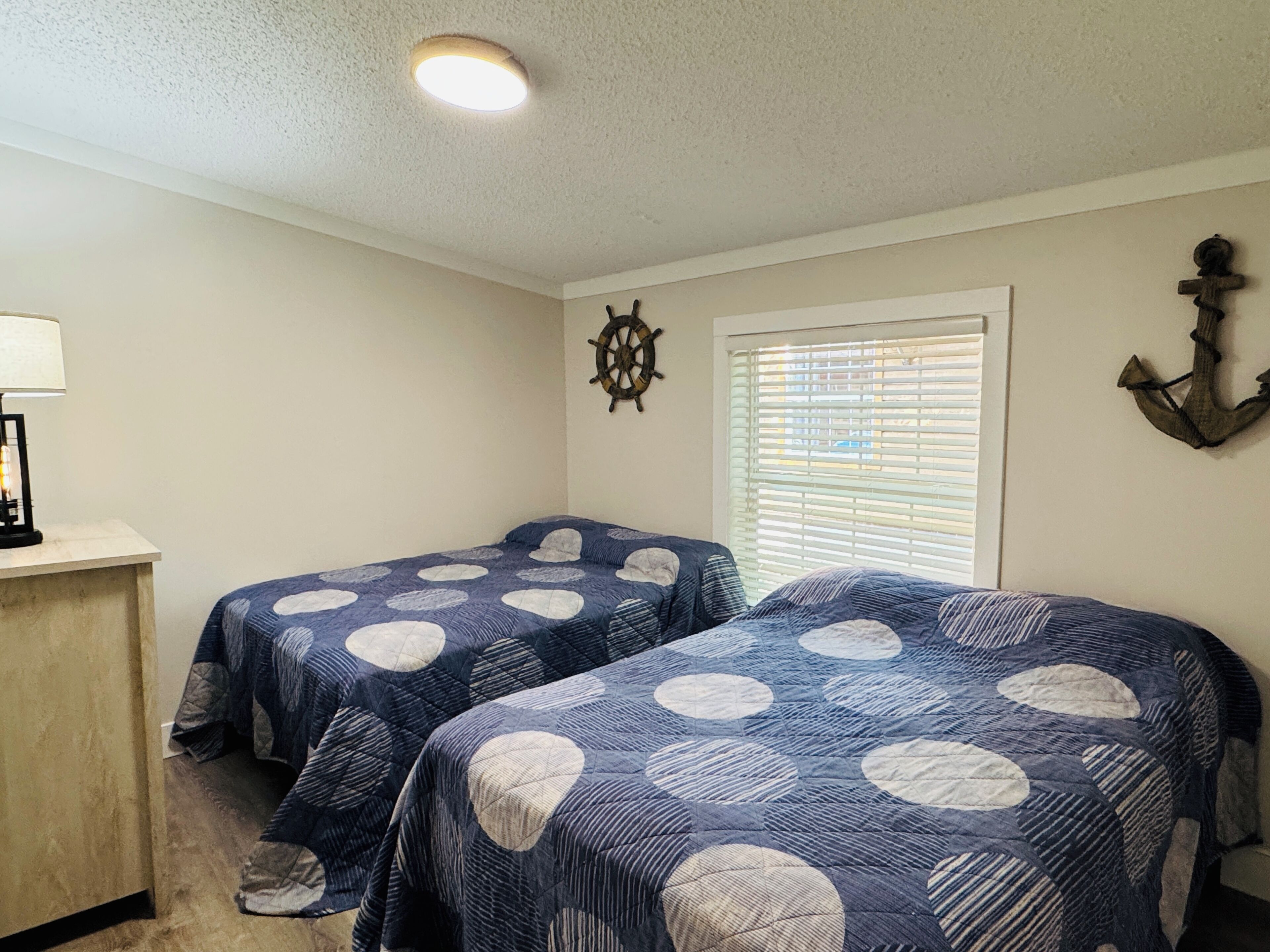 Une chambre avec deux lits, un bureau, un gouvernail de bateau et un élément de décoration en forme d’ancre.