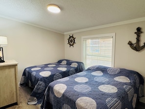 A bedroom with two beds, a desk, a ship's wheel, and an anchor decoration.