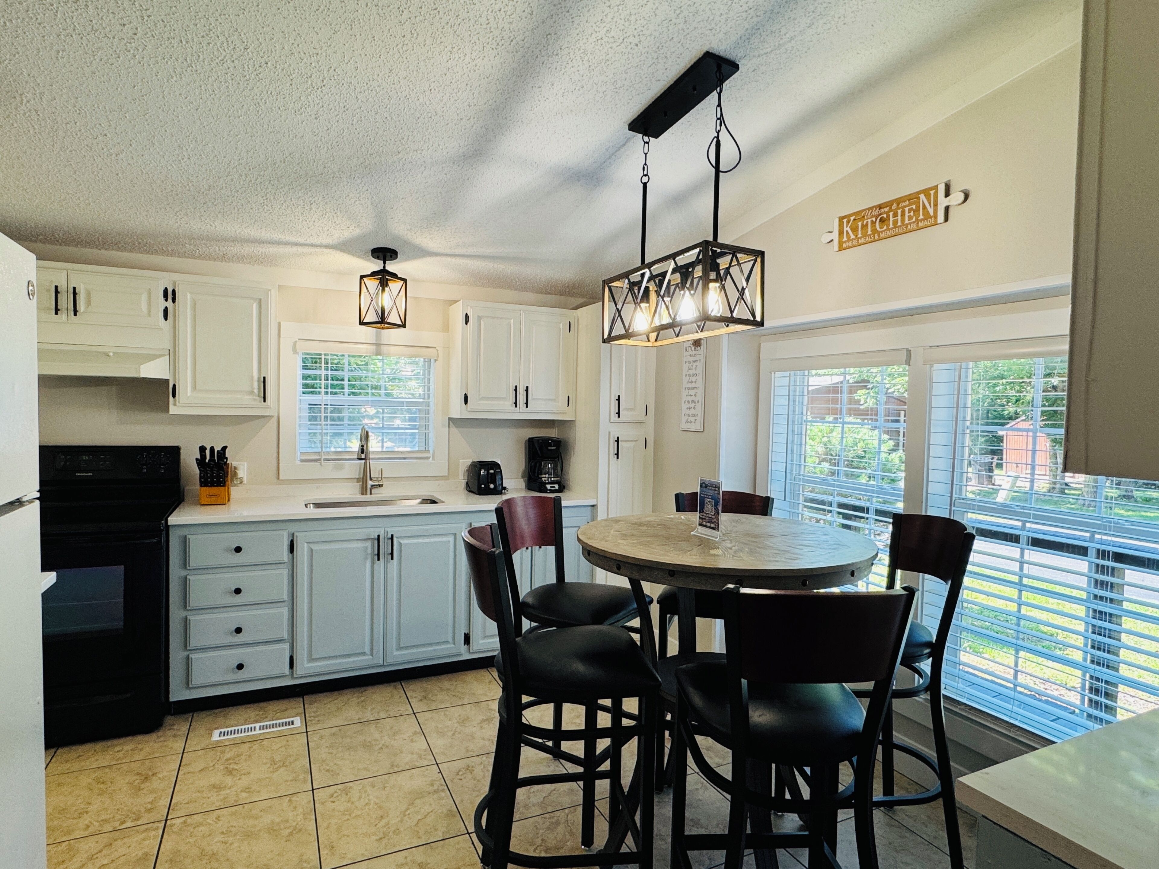 A kitchen with white cabinets, a black stove, a dining table with four chairs, and a hanging light fixture.