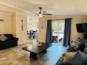 A living room with a black sofa, a coffee table, a ceiling fan, and a view of the outdoor patio area. - Easy Stay w/ 2 Parking Spots | 8 ppl | IC83 (Put-in-Bay)