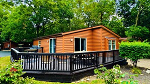 Une petite cabane en bois d’un seul étage, dotée d’une terrasse et d’un garage, et entourée d’une végétation luxuriante.