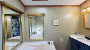 Une salle de bain avec une grande baignoire, deux miroirs avec des cadres dorés, un lavabo et une douche.