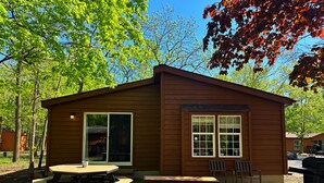 A small wooden cabin with a picnic table and benches, surrounded by trees. - Chill & Cozy Back Escape—Grill Time | 8 ppl | IC99 (Put-in-Bay)