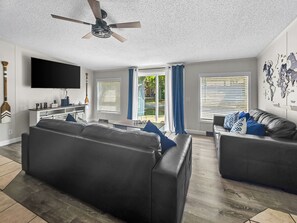 A living room with a flat-screen TV, two sofas, a ceiling fan, and a world map on the wall.