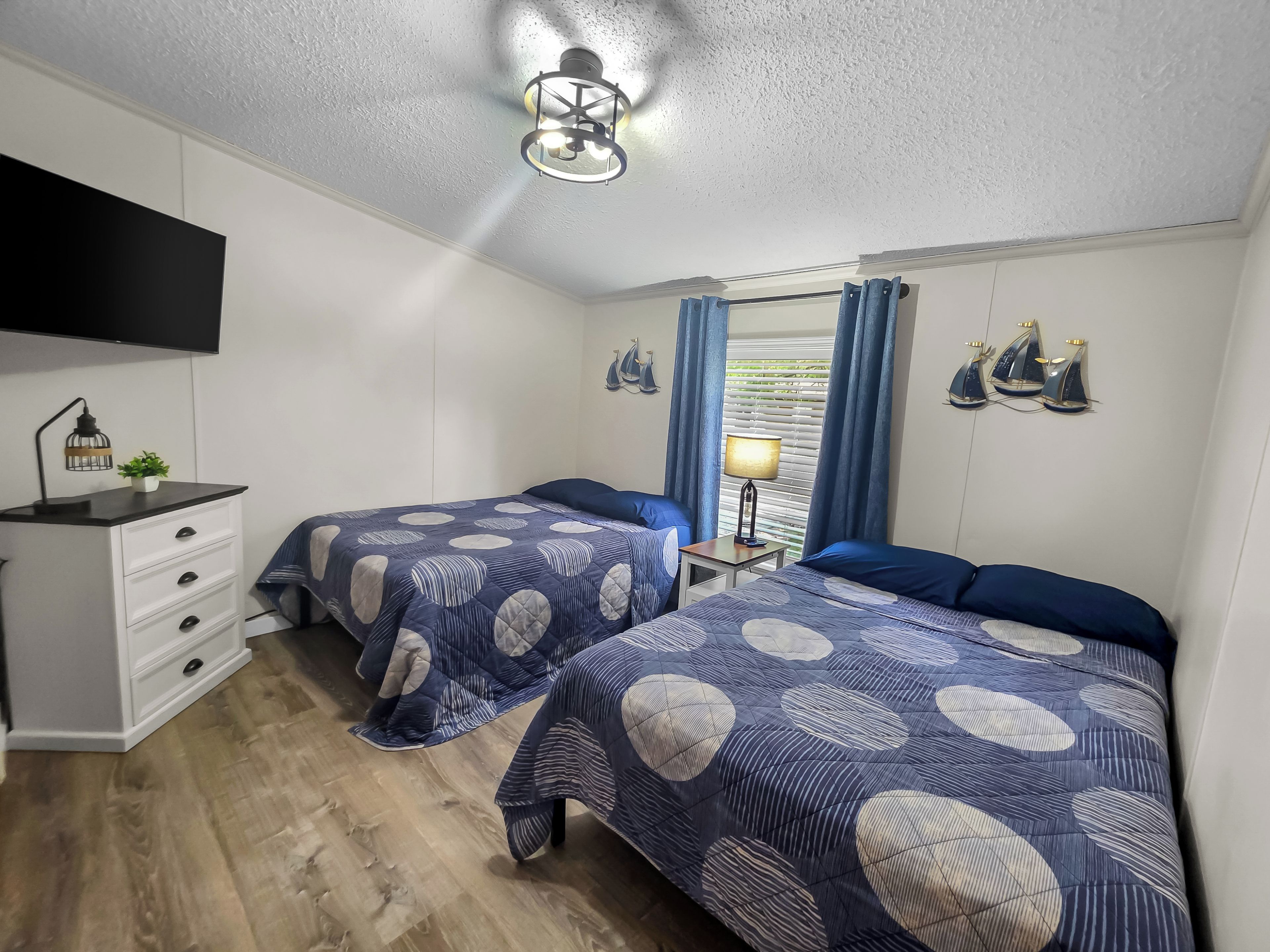 A bedroom with two beds, a dresser, a TV, a lamp, and a window with curtains.