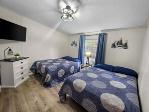 Une chambre avec deux lits, une commode, une télévision, une lampe et une fenêtre avec des rideaux.