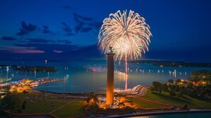 Un grand feu d’artifice illuminant une étendue d’eau, avec une tour imposante en premier plan.