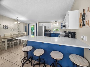 Una cocina moderna con una isla central, taburetes de bar y un comedor con mesa y sillas.