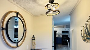 Un couloir avec un banc en bois, un miroir rond, une petite décoration représentant un phare et un luminaire moderne.