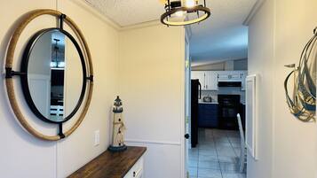 A hallway with a wooden bench, a round mirror, a small lighthouse decoration, and a modern light fixture.