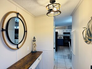 Un couloir avec un banc en bois, un miroir rond, une petite décoration représentant un phare et un luminaire moderne.