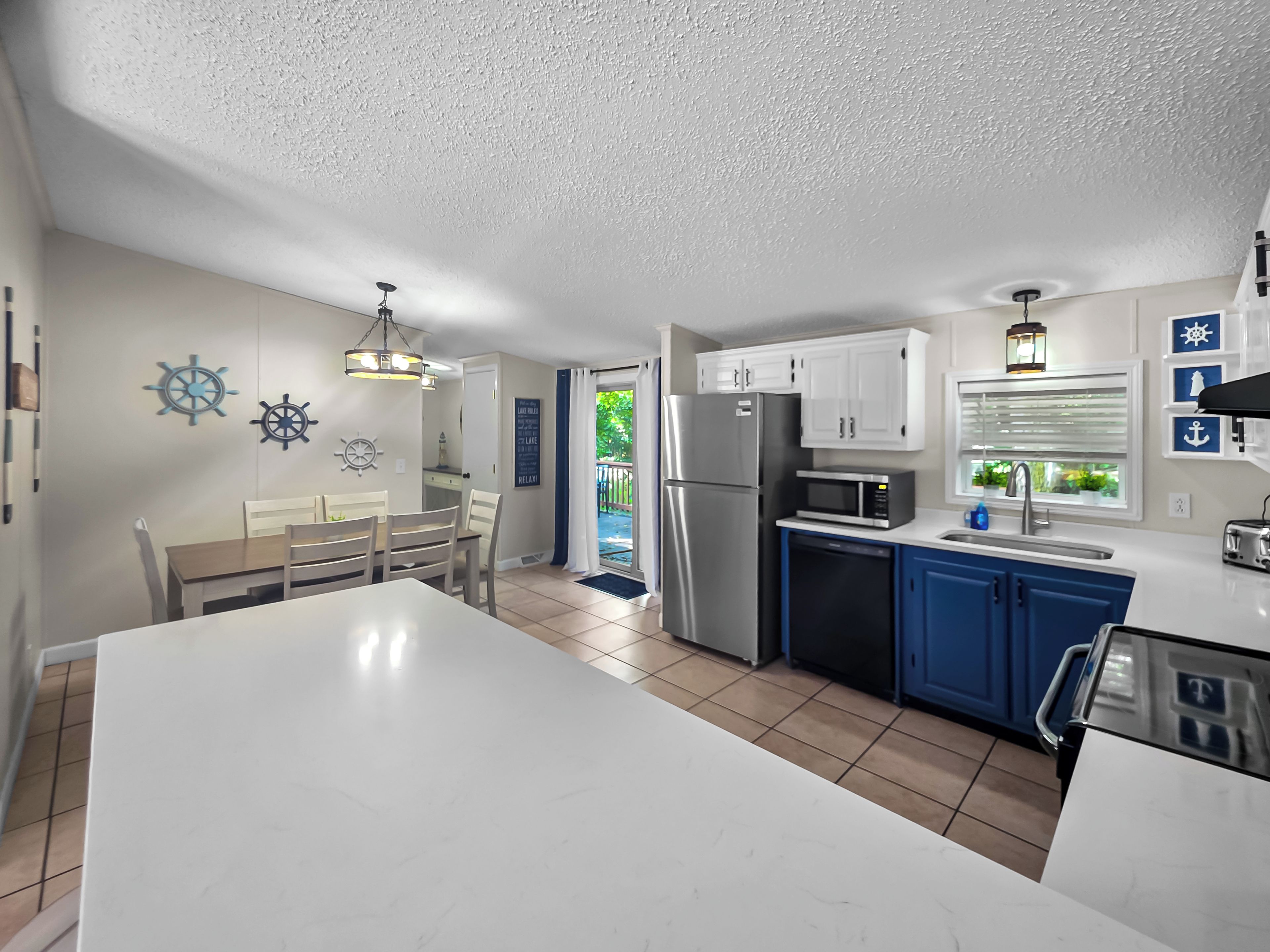 A kitchen with a central island, a dining area with a table and chairs, and a view of the outdoors.