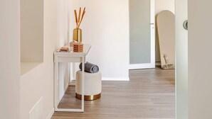 Un couloir avec une table blanche, un pouf rond et une porte donnant sur une autre pièce.