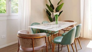Un coin repas avec une table en marbre, des chaises vertes et un vase rempli de fleurs.
