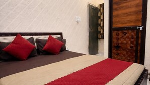 A bedroom with a bed, pillows, a red blanket, a wooden door, and an air conditioning unit. - SRT Homes (Ranchi)