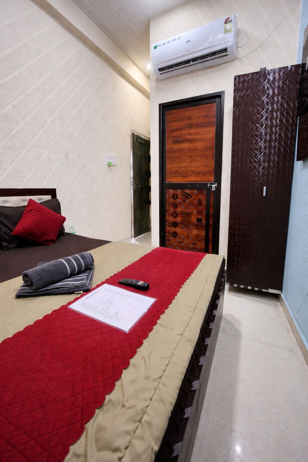 Une chambre d’hôtel avec un lit, une couette rouge, une télécommande et une porte ornée d’un motif.