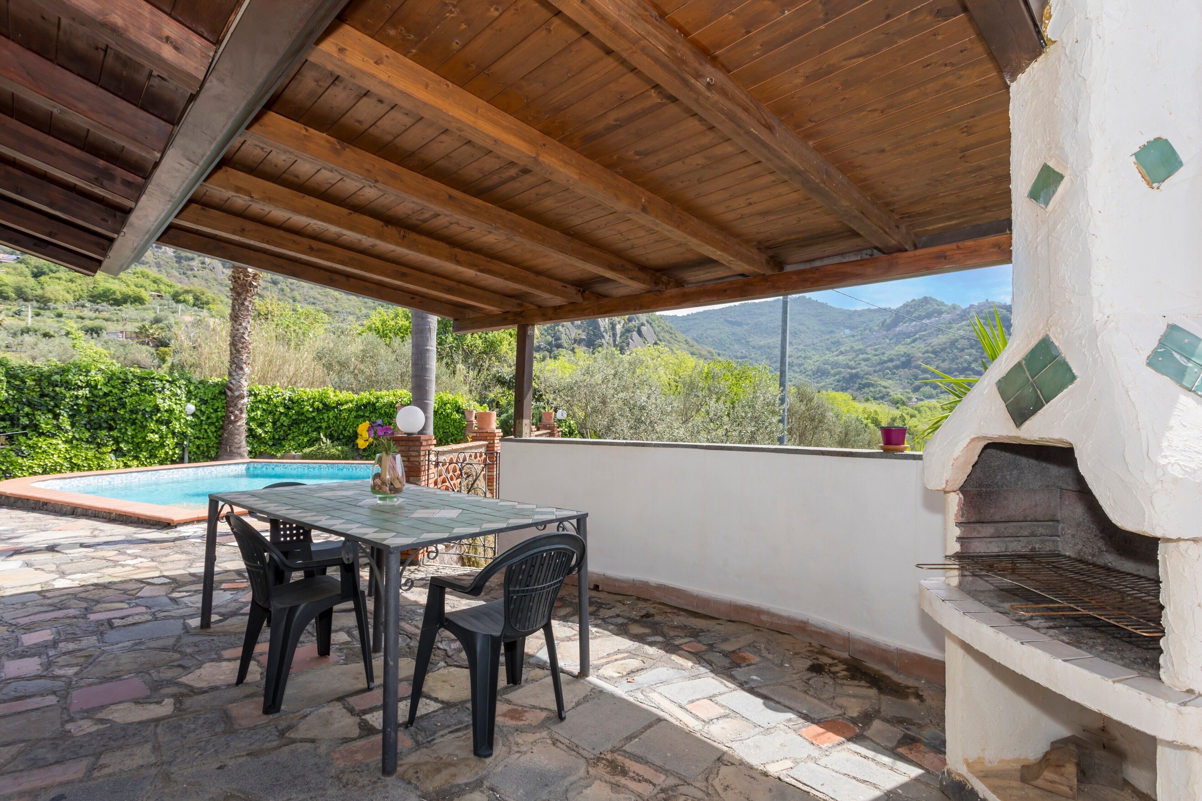 A covered patio with a pool, outdoor table and chairs, and a stone-tiled floor.