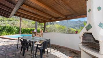 Un patio couvert avec une piscine, une table et des chaises d’extérieur, et un sol carrelé en pierre.