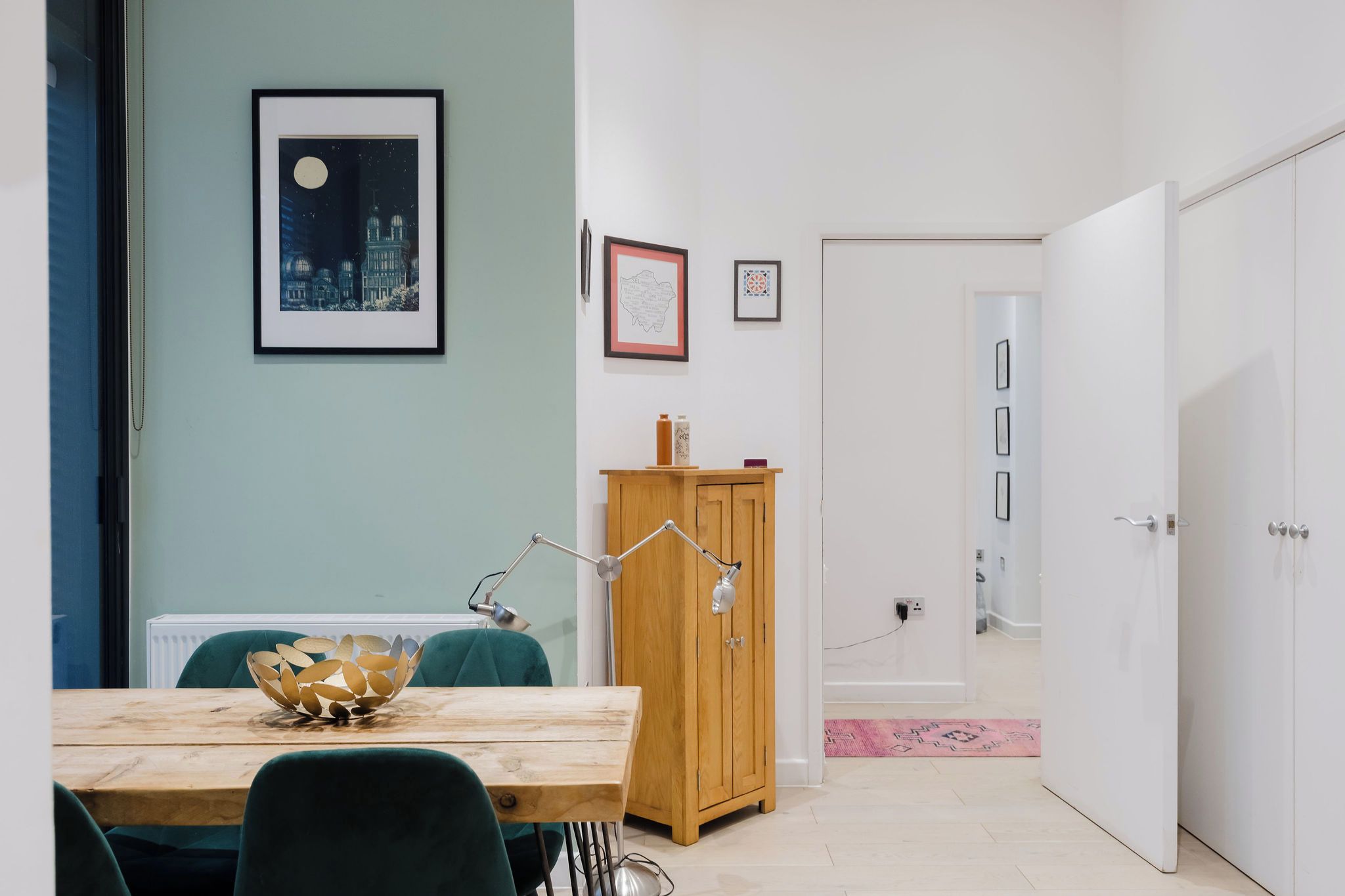 A room with a wooden dining table, chairs, a cabinet, and a door leading to another room.