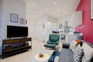 A modern living room with a flat-screen TV, a green armchair, a grey sofa, and a kitchen area in the background. - Tasteful 2BD Canalside Hideaway in Hackney (Greater London)