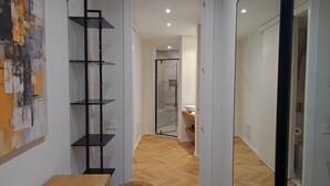 A modern interior with a wooden floor, a black shelving unit, and a bathroom visible through an open door. - Center Suite Cagliari (Cagliari)