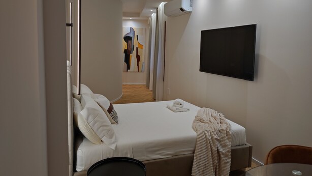 A hotel room with a bed, a TV, a small table, and a chair. - Center Suite Cagliari (Cagliari)