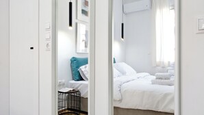A modern bedroom with a large mirror, a bed with white bedding, a grey sofa, and a black hanging light fixture. - Spacious 3-Bedroom Retreat in the Heart of Pagrati (Athina)