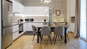 A modern kitchen with white cabinetry, stainless steel appliances, and a herringbone wood floor. - Spacious 3-Bedroom Retreat in the Heart of Pagrati (Athina)