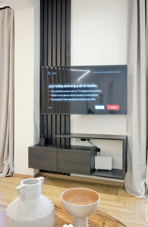 Een moderne woonkamer met een flatscreen televisie aan de wand, een donker houten console eronder, en een witte vaas en schaal op de vloer.