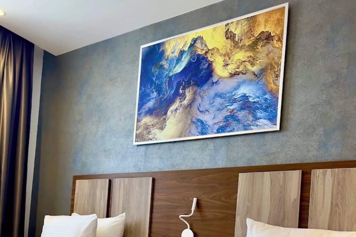 Ein Hotelzimmer mit zwei Betten, einem großen abstrakten Gemälde an der Wand und einer Uhr am Kopfteil.