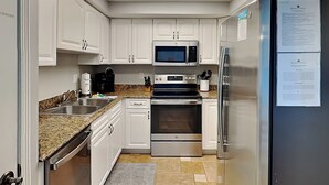 A modern kitchen with white cabinets, a stainless steel refrigerator, a microwave, an oven, and a coffee maker. - Regency Towers #407 East | Pet Friendly, Beach Service, Pool, Pickleball (Pensacola Beach)