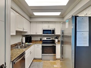 Eine moderne Küche mit weißen Schränken, einem Edelstahlkühlschrank, einer Mikrowelle, einem Backofen und einer Kaffeemaschine.