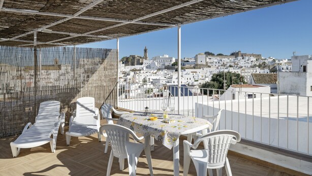 A terrace with a table and chairs, a view of a white town with buildings and a tower, and a clear sky. - Belvedere Apartment with Views of Vejer’s Historic Old Town (Vejer de la Frontera)