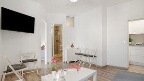 A modern living room with a flat-screen TV, a dining table with chairs, a sofa, and a kitchen area with cabinets. - Belvedere Apartment with Views of Vejer’s Historic Old Town (Vejer de la Frontera)