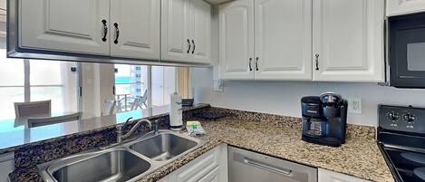 A modern kitchen with white cabinets, granite countertops, a stainless steel sink, a coffee maker, and a microwave.