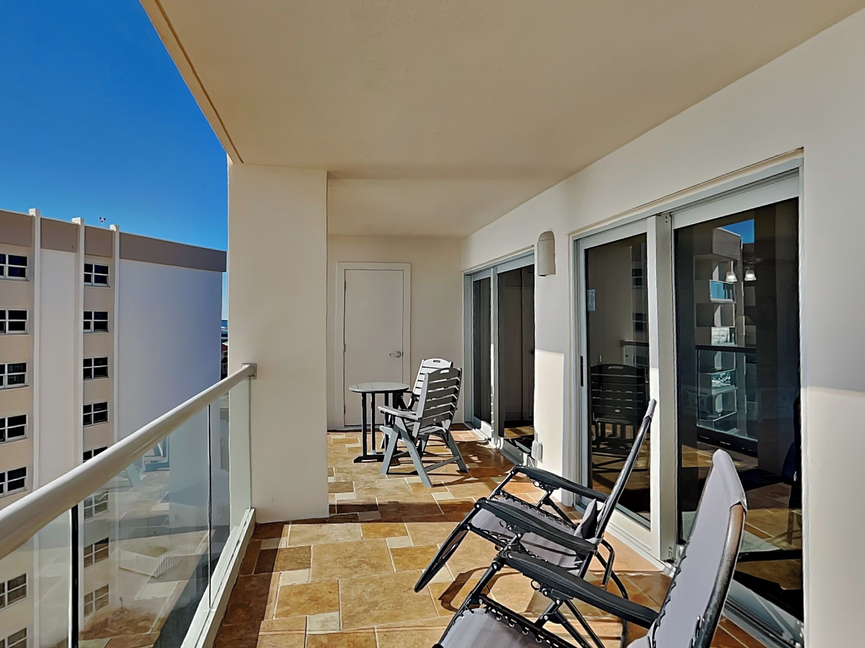 Un balcon doté d’une balustrade en verre, d’une porte blanche et d’un sol carrelé.