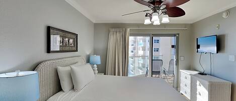 A hotel room with a large bed, a ceiling fan, a TV, and a balcony with a view of buildings.